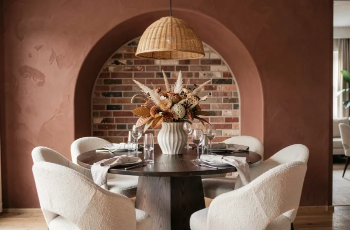 Salle à manger moderne avec chaises boucle, table en chêne fumé et décor botanique séché sous une arche en plâtre argile tendance intérieur 2025